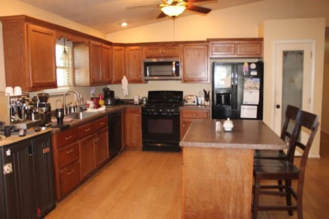 kitchen with lofted ceiling, light wood-style flooring, a kitchen breakfast bar, black appliances, and a sink