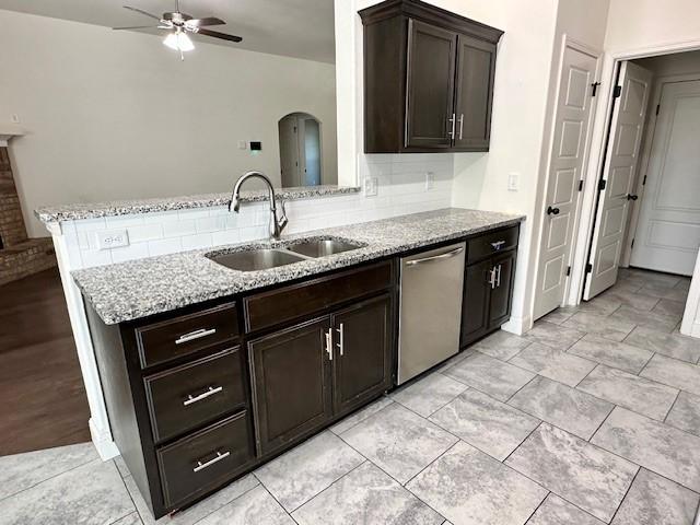 kitchen with arched walkways, stainless steel dishwasher, a sink, and light stone counters