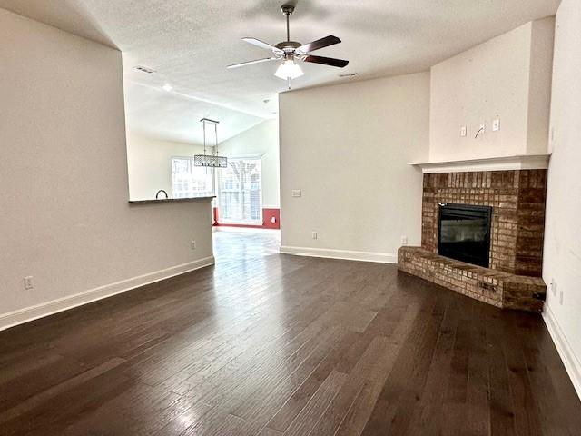 unfurnished living room with baseboards, dark wood finished floors, lofted ceiling, a fireplace, and ceiling fan with notable chandelier