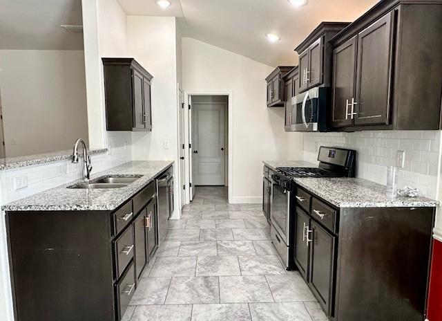 kitchen featuring vaulted ceiling, light stone counters, stainless steel appliances, and a sink