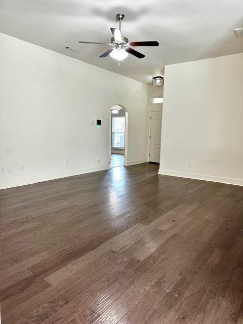 empty room featuring arched walkways, dark wood-type flooring, a ceiling fan, and baseboards