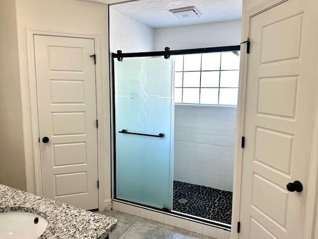 bathroom featuring a shower stall, visible vents, a textured ceiling, and vanity