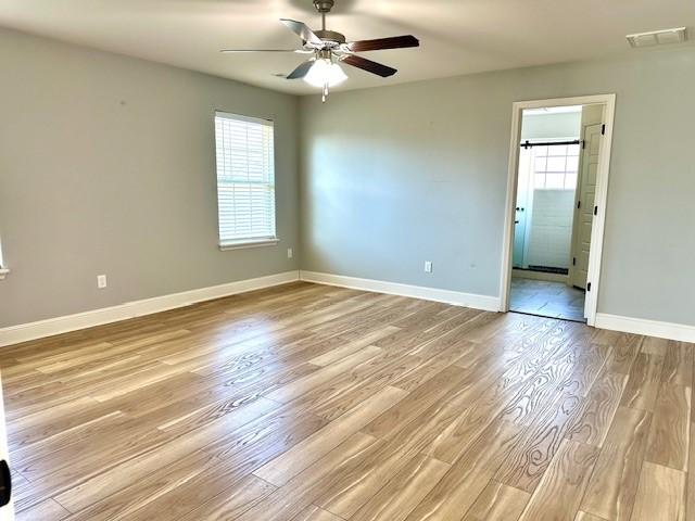 unfurnished room with a ceiling fan, light wood-type flooring, visible vents, and baseboards