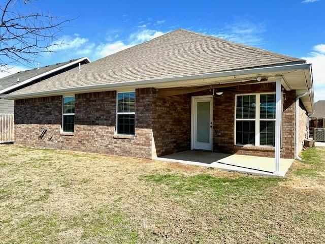 back of property with brick siding, a lawn, a patio, and roof with shingles