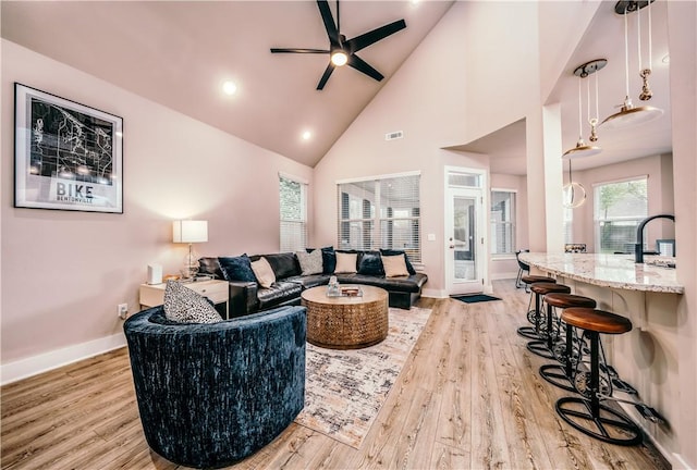 living room featuring light wood-style floors, visible vents, baseboards, and high vaulted ceiling