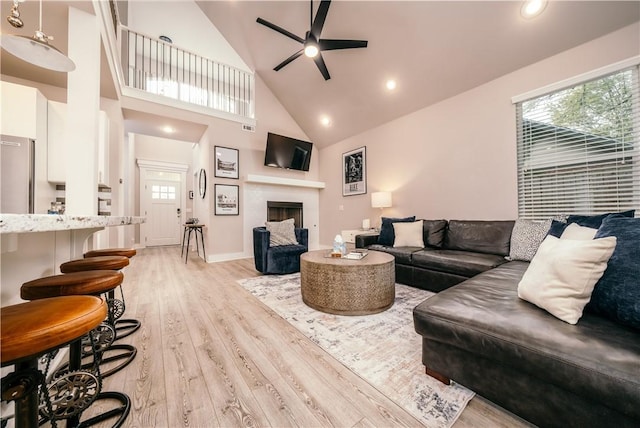 living room with ceiling fan, high vaulted ceiling, a fireplace, baseboards, and light wood finished floors