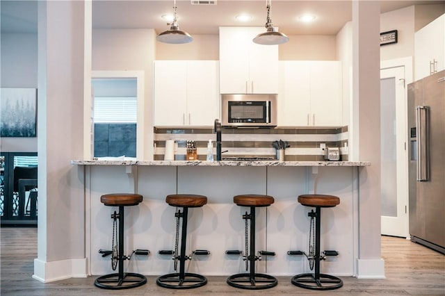 kitchen with light wood finished floors, appliances with stainless steel finishes, hanging light fixtures, a kitchen bar, and white cabinetry