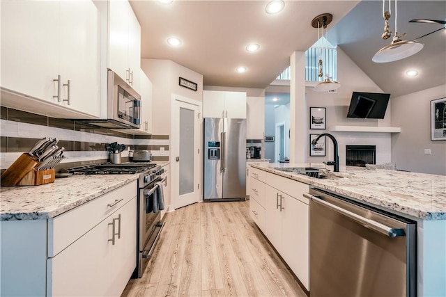 kitchen with a fireplace, stainless steel appliances, light wood-style floors, white cabinetry, and a sink