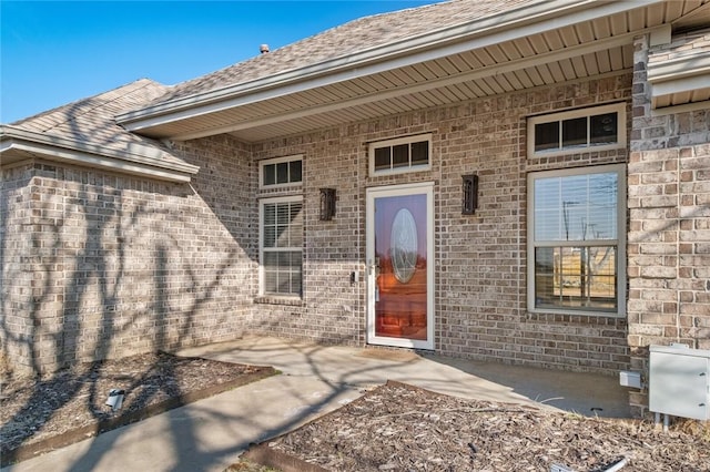 doorway to property featuring brick siding and roof with shingles