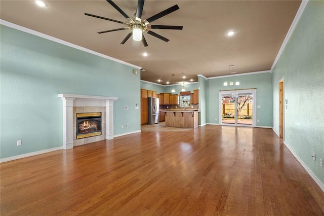 unfurnished living room with ceiling fan, wood finished floors, a tile fireplace, and baseboards