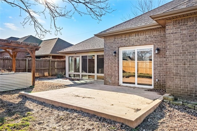 rear view of property featuring roof with shingles, brick siding, fence, and a patio