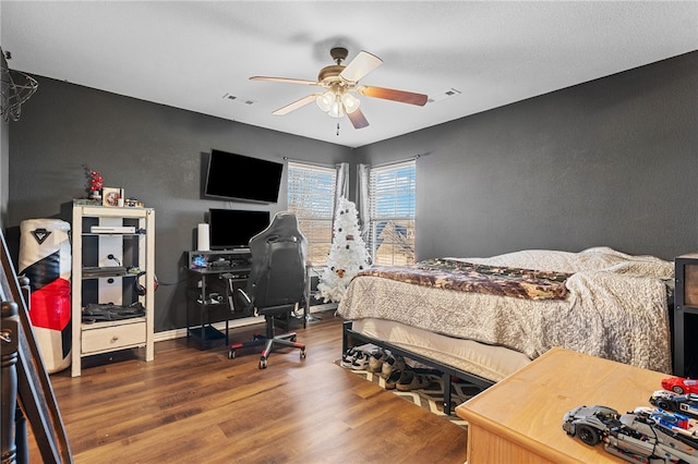 bedroom with a ceiling fan, visible vents, baseboards, and wood finished floors