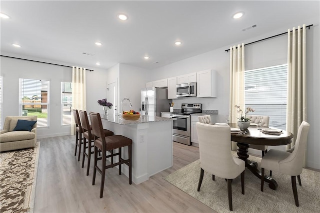 kitchen featuring a breakfast bar area, stainless steel appliances, visible vents, light wood-style floors, and white cabinetry