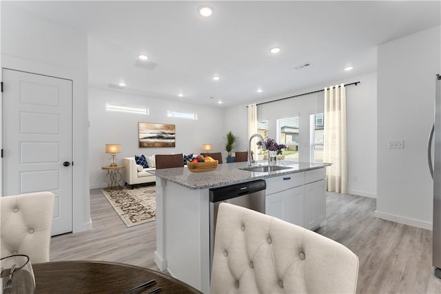 kitchen with light stone counters, recessed lighting, a sink, light wood-style floors, and a center island with sink