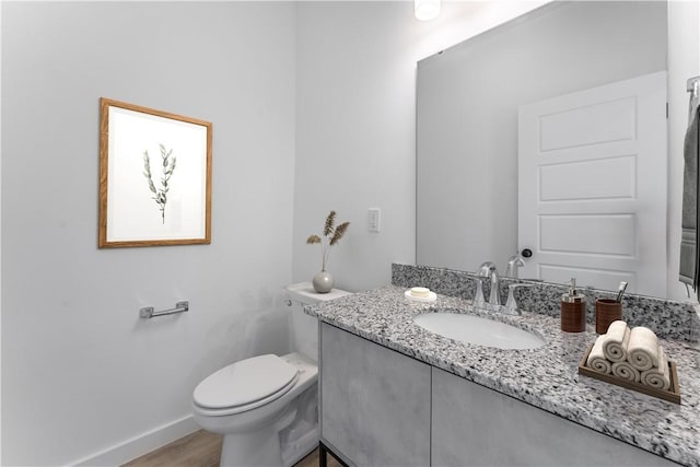 half bathroom with wood finished floors, vanity, toilet, and baseboards