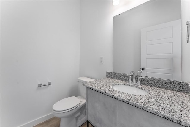 half bath with wood finished floors, vanity, toilet, and baseboards