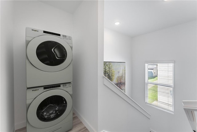 clothes washing area with laundry area, baseboards, stacked washer / dryer, and wood finished floors