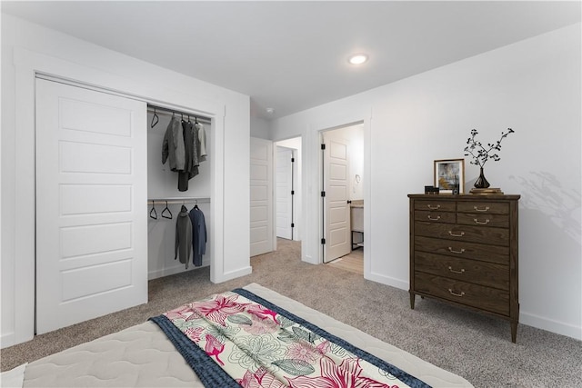 carpeted bedroom featuring a closet, ensuite bath, and baseboards