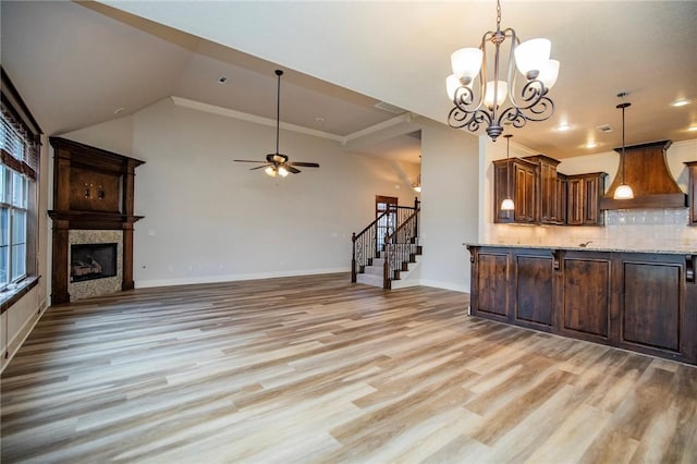 kitchen with light stone counters, a fireplace, light wood finished floors, backsplash, and premium range hood