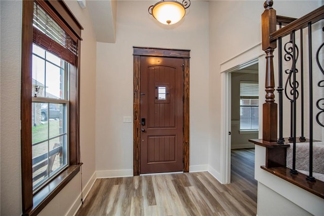 foyer entrance with stairs, light wood finished floors, and baseboards