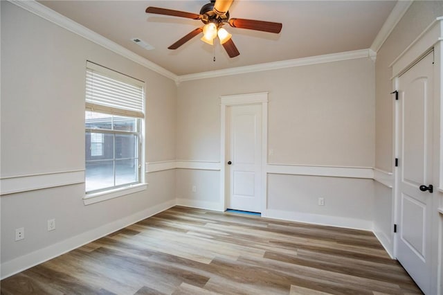 spare room with ceiling fan, wood finished floors, visible vents, baseboards, and crown molding