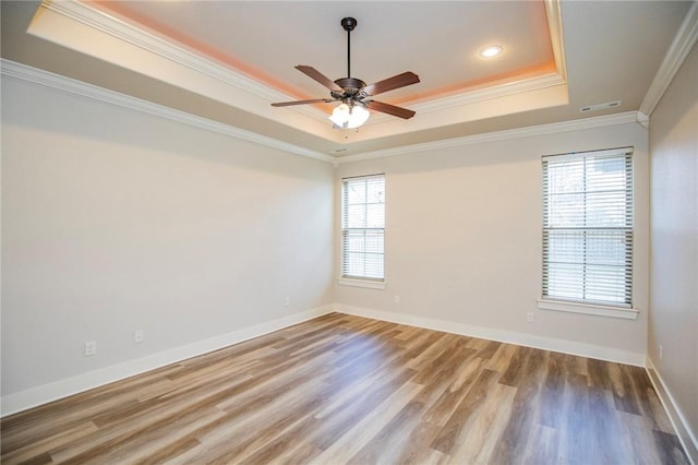 spare room with crown molding, visible vents, a raised ceiling, and wood finished floors