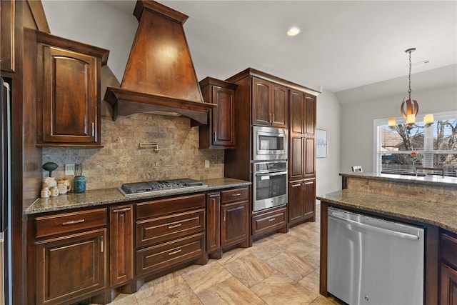 kitchen with tasteful backsplash, custom range hood, hanging light fixtures, appliances with stainless steel finishes, and vaulted ceiling