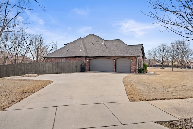 view of home's exterior featuring driveway, a shingled roof, an attached garage, fence, and brick siding