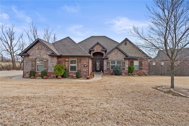 craftsman-style house featuring a shingled roof, a front yard, brick siding, and fence