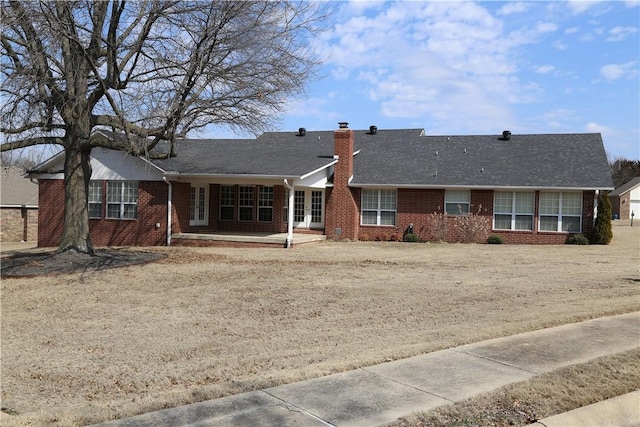 back of property with french doors, brick siding, a chimney, and roof with shingles