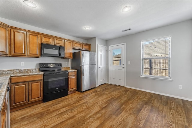 kitchen featuring black appliances, brown cabinetry, wood finished floors, and baseboards