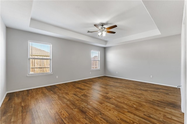 spare room featuring a ceiling fan, a tray ceiling, baseboards, and wood finished floors