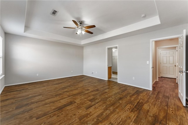 unfurnished bedroom featuring visible vents, dark wood finished floors, baseboards, ceiling fan, and a tray ceiling