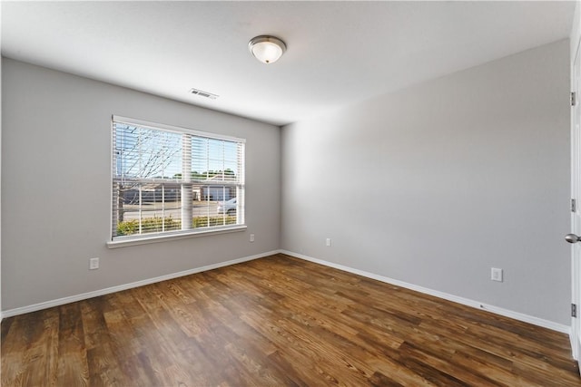 spare room featuring dark wood-style flooring, visible vents, and baseboards