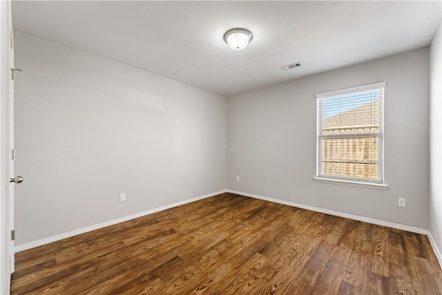 empty room featuring dark wood-style floors, baseboards, and visible vents