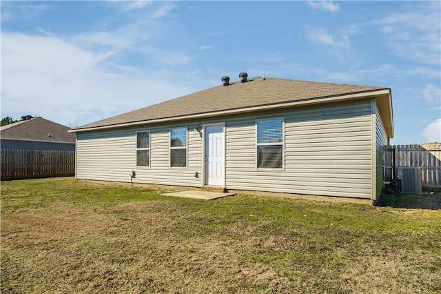 rear view of property with central AC unit, a shingled roof, fence, and a yard