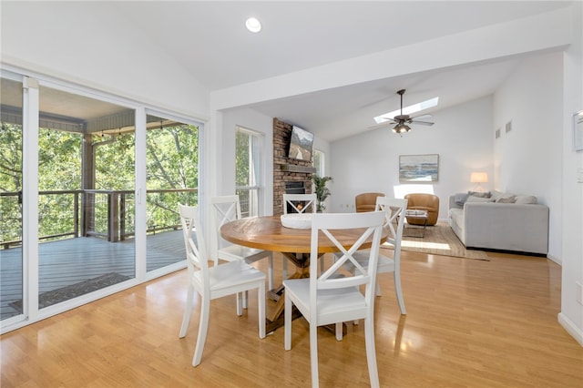 dining area with light wood-type flooring, plenty of natural light, a fireplace, and vaulted ceiling