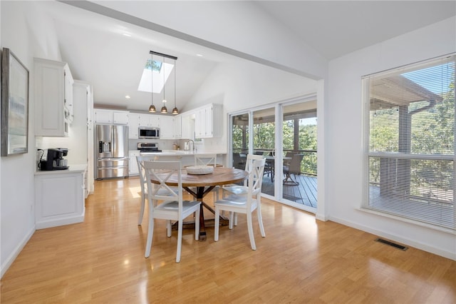 dining space with light wood finished floors, vaulted ceiling with skylight, and visible vents