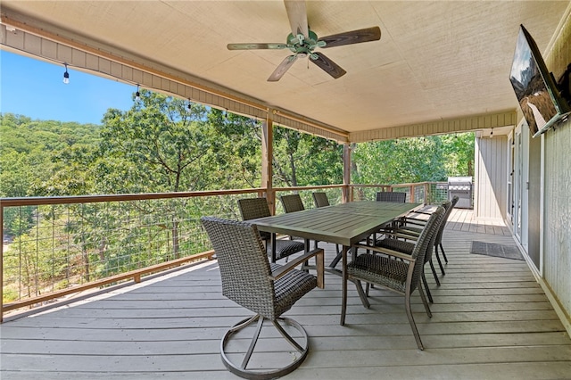 deck with a forest view, ceiling fan, outdoor dining area, and grilling area