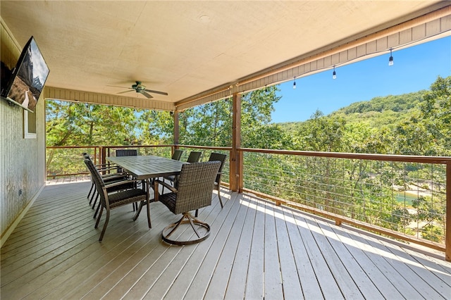 wooden terrace featuring a forest view, outdoor dining space, and a ceiling fan