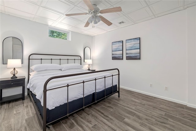 bedroom with ceiling fan, wood finished floors, visible vents, baseboards, and an ornate ceiling