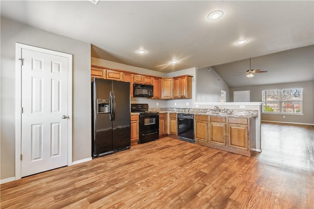 kitchen with brown cabinetry, light wood finished floors, black appliances, and a peninsula