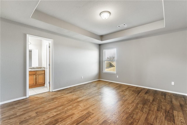 spare room featuring light wood finished floors, baseboards, visible vents, and a tray ceiling