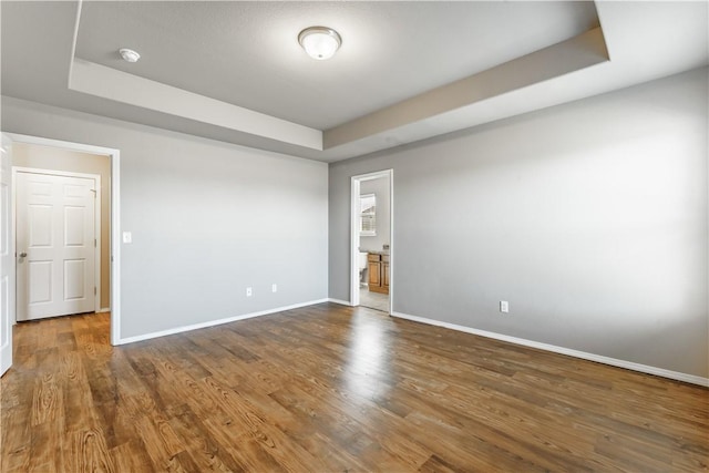 unfurnished room featuring a tray ceiling, baseboards, and wood finished floors