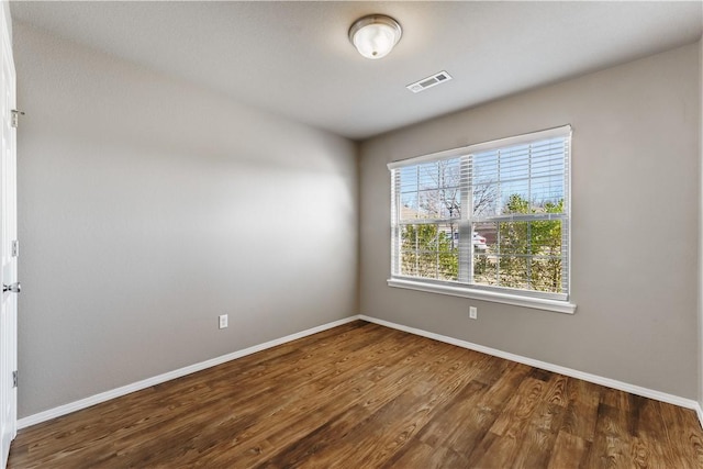 spare room with baseboards, visible vents, and wood finished floors