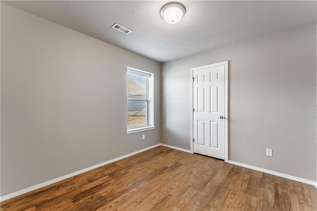 empty room featuring wood finished floors, visible vents, and baseboards