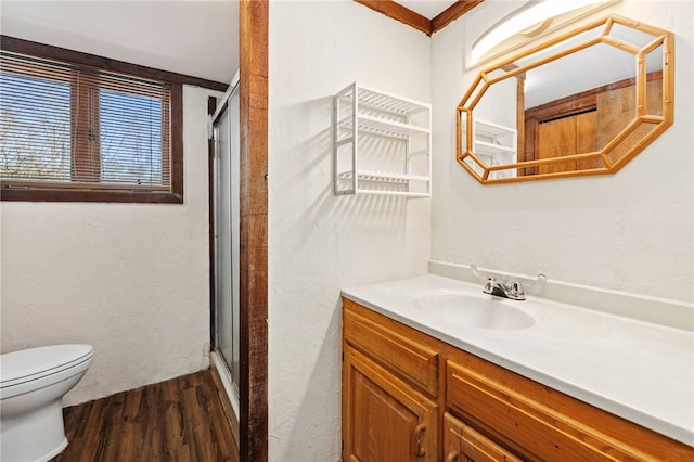 bathroom featuring a textured wall, toilet, wood finished floors, vanity, and a shower stall