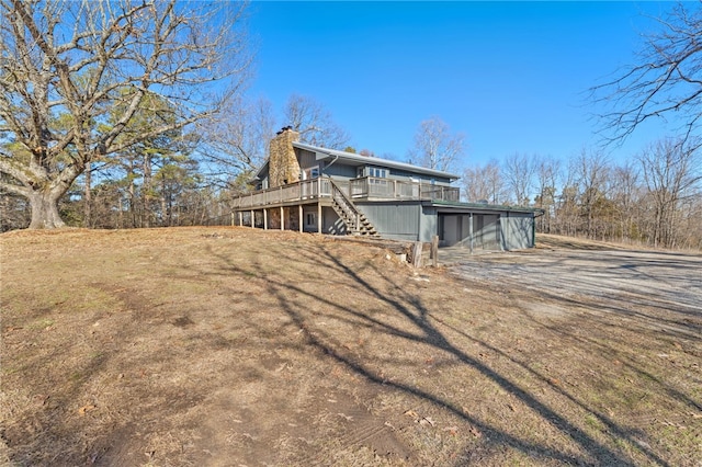 view of side of property with driveway, stairway, a chimney, and a wooden deck