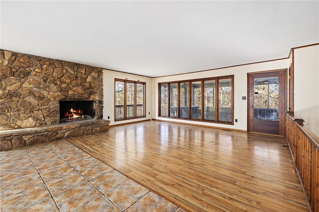 unfurnished living room with a stone fireplace, wood finished floors, and baseboards