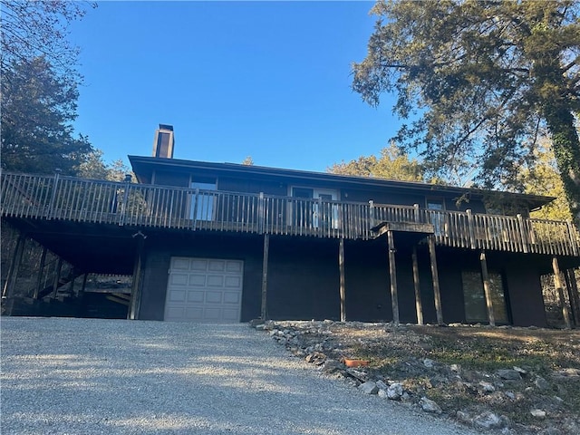 rear view of property with a deck, a carport, a chimney, and driveway